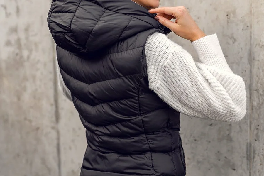 Kobieta ubrana w czarną puchową kamizelkę i biały sweter.